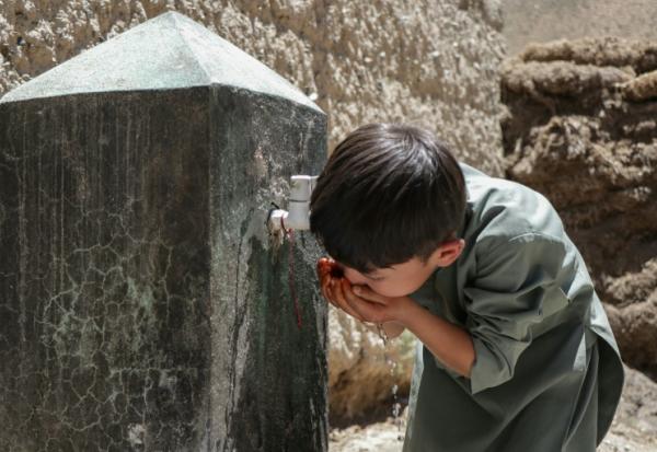 Un enfant boit de l'eau au robinet d'une fontaine à Qavariyak, dans la province de Bamiyan, le 18 juin 2025 en Afghanistan