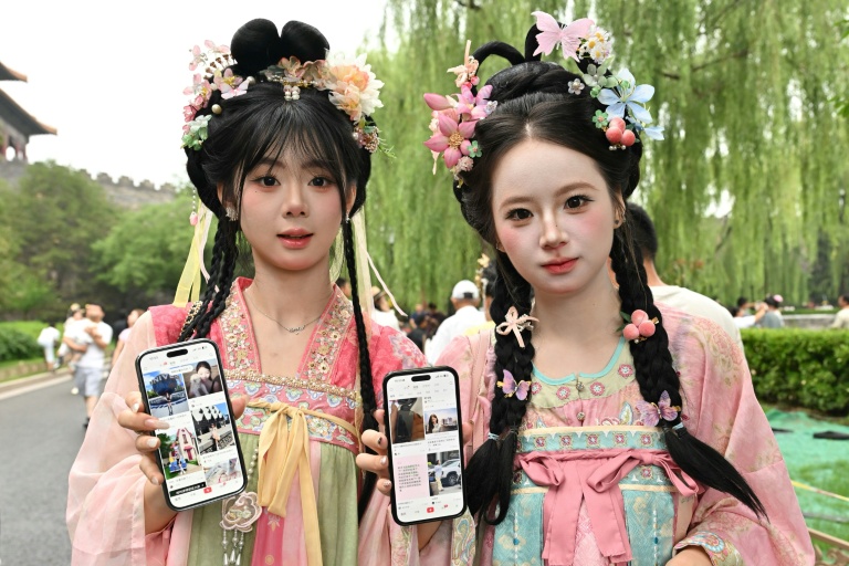 Des touristes originaires de la province de Jilin, dans le nord-est de la Chine, montrent leurs comptes Xiaohongshu sur leurs téléphones alors qu'elles visitent la Cité interdite à Pékin, le 11 juillet 2026