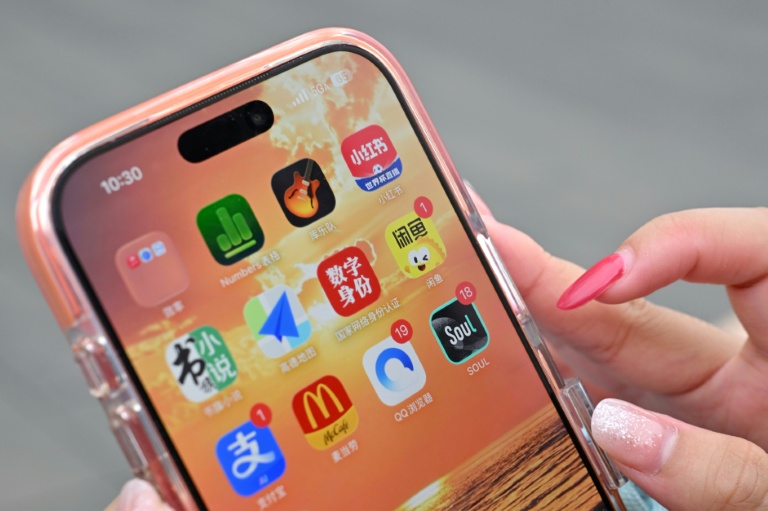 Une utilisatrice de Xiaohongshu se prépare à ouvrir l'application chinoise (en haut à droite) alors qu'elle visite la Cité interdite à Pékin, le 11 juillet 2026